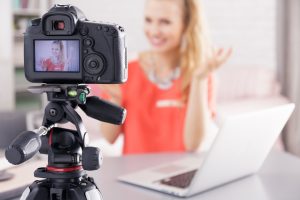 Woman sitting beside desk with laptop while filming her broadcast