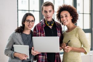 Young cheerful team of three people watching a video or looking over a business presentation on laptop in the office